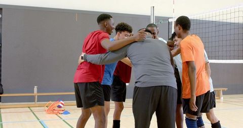 Multiethnic male volleyball team huddling with coach in indoor gym court showing teamwork