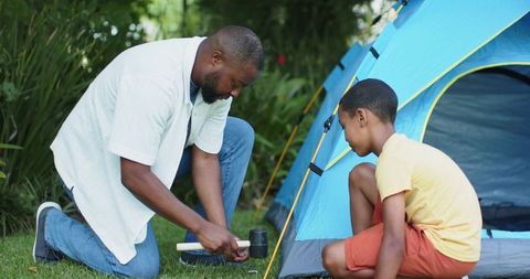 African american father and son building backyard tent together for family camping