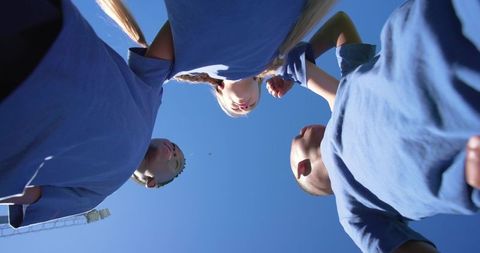 Diverse teen sports team huddling under clear blue sky in matching blue shirts