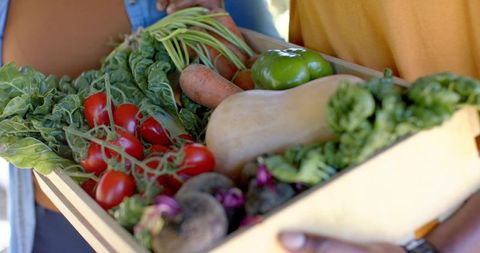 African american couple holding crate of fresh organic vegetables at farmers market