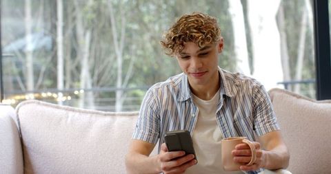 Relaxed guy enjoying a coffee while browsing on smartphone