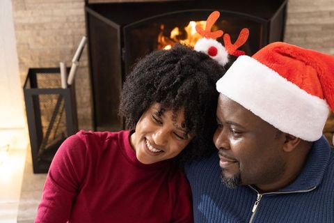 African american couple enjoying cozy christmas by fireplace wearing santa hat and antlers
