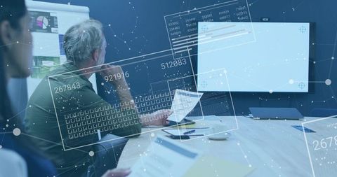 Mature Professional Collaborating with Team Using Data Overlays and Analytics in Boardroom
