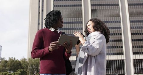 Diverse coworkers discussing project in urban plaza with tablet and backpack