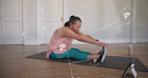 Chinese senior woman stretching at home with tablet and wireless wearable fitness tracking
