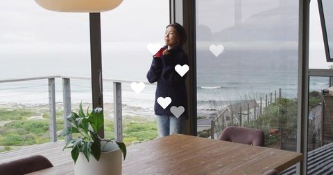 Woman standing on coastal balcony gazing at ocean through glass doors, serene interior