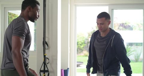 Diverse male partners training with trx suspension straps in sunlit home gym backyard