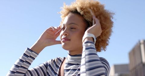 African American woman adjusting hair wearing smartwatch and striped top in urban portrait
