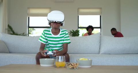 African American Boy Wearing VR Headset Playing Video Game on Couch with Parents Nearby