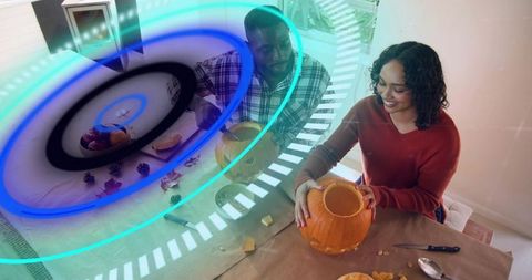 Couple carving pumpkins together on dining table with cozy fall decor and holographic overlay