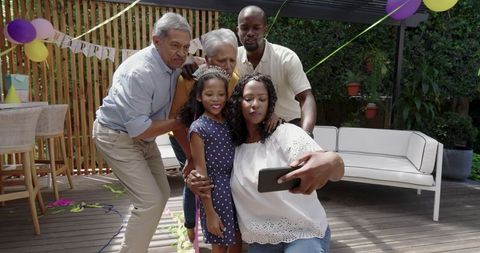 Multigenerational family taking selfie at backyard birthday party with balloons and banner