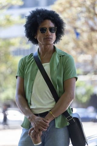 African man standing on urban street wearing green shirt sunglasses messenger bag with coffee