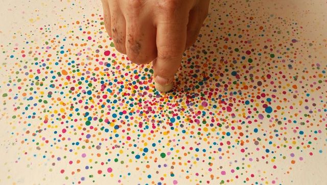 Hand pressing sponge dabbing vibrant multicolor dot pattern on paper creating playful confetti art