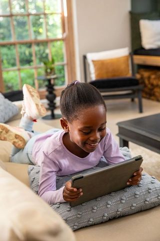 African american girl lying on couch using tablet smiling in sunlit cozy living room