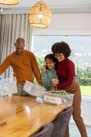 Diverse family sorting recyclables at dining table with labeled bins and egg carton
