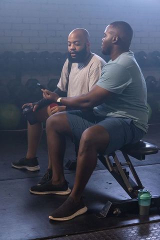 African american men sharing workout app on smartphone while resting on bench at gym