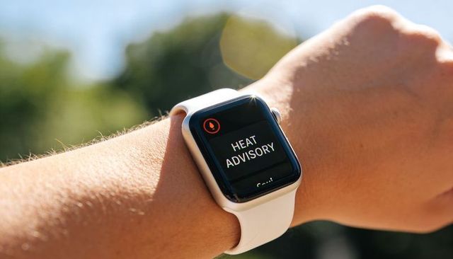 Smartwatch showing heat advisory alert on wrist with white silicone band in sunny outdoor bokeh