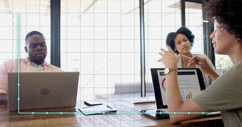 Woman leading team meeting in glass office with laptops and data-driven charts