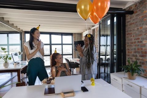 Team celebrating birthday in modern office with balloons and cupcakes