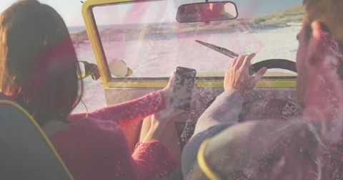 Couple driving yellow beach buggy holding smartphone enjoying seaside adventure roadtrip