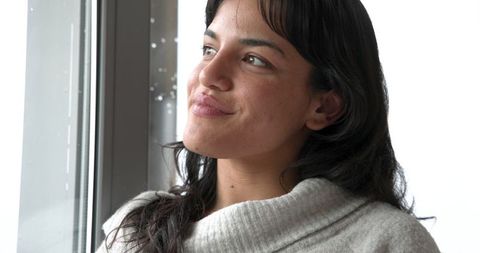 Woman Contemplates by Rain-Speckled Window in Minimalistic Setting