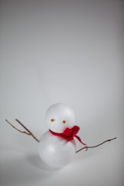 Miniature Christmas snowman ornament with twig arms and red scarf. Sitting against plain white background, ideal for minimalist holiday decorations. Great for use in seasonal advertising, Christmas themed projects, or winter craft ideas.