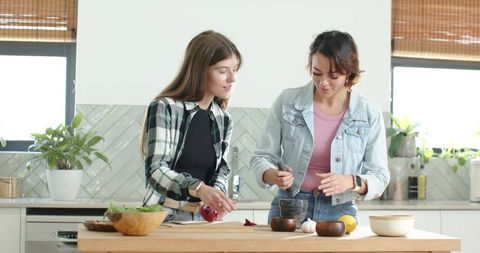 Diverse friends preparing fresh meal using mortar and pestle on bright kitchen island