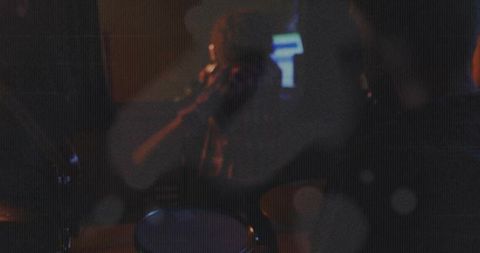 Female vocalist performing in intimate neon club with drum kit and grainy atmosphere