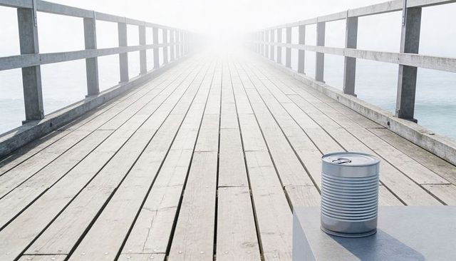 Foggy wooden pier stretching into bright mist with metal tin can on foreground plinth