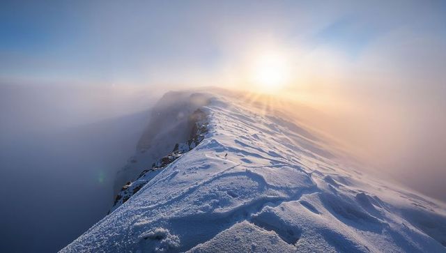 Sunlit Snow Ridge Leading to Misty Alpine Horizon with Footprints