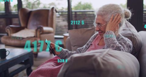 Senior woman using smartphone on sofa viewing digital currency overlays for finance