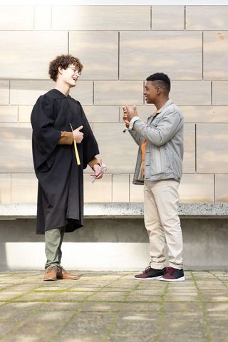 Graduating student celebrating with friend on campus courtyard holding diploma and phone