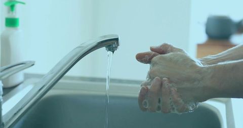 Person Washing Hands under Running Water with Soap at Home Sink