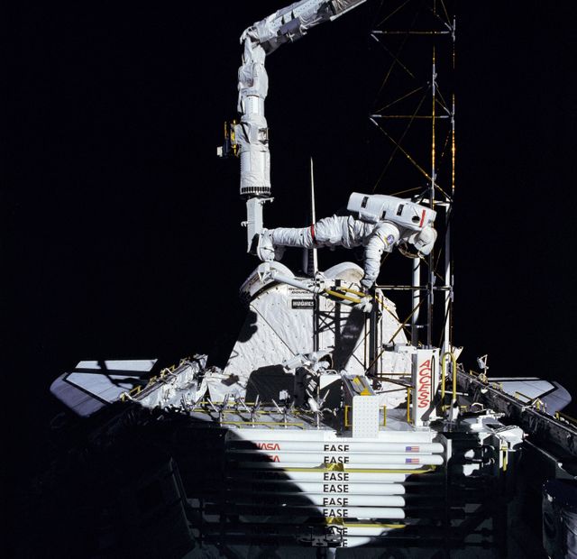Astronaut conducting assembly operations on experimental satellite structure during Extravehicular Activity (EVA) on NASA's STS-61B Space Shuttle Atlantis mission. Ideal for educational materials on space exploration, NASA missions, or engineering tasks in space. Can also be used to illustrate astronaut activities and satellite technologies.