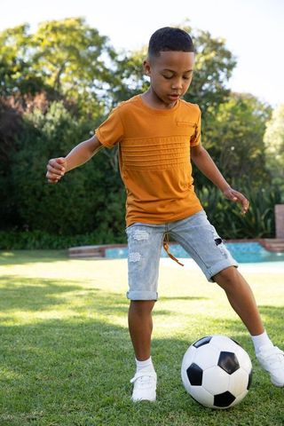 Young Boy Having Fun Playing Soccer On Sunny Lawn
