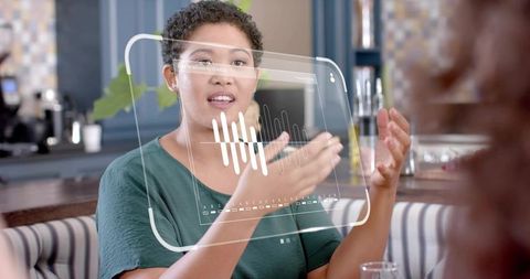 Woman gesturing while speaking with holographic audio waveform interface in cafe booth