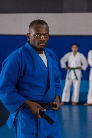 Martial arts instructor adjusting belt amid teens in training dojo