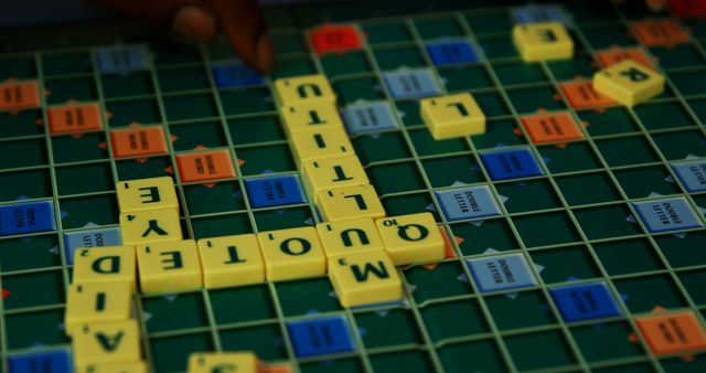 A close-up view of a Scrabble game board in progress, with a hand placing letter tiles, with copy space. Scrabble is a popular word-based board game that challenges players to create words and score points based on letter values.