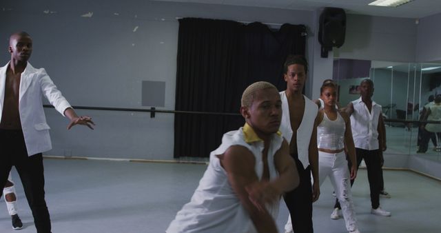 Group of young, diverse dancers practicing contemporary dance moves in studio wearing coordinated outfits. Ideal for content regarding dance rehearsals, collective creativity, teamwork, or cultural arts.