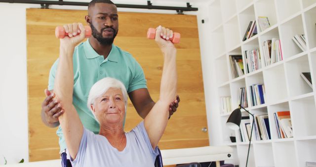 Image of african american male physiotherapist exercising with caucasian senior woman. seniors health and nursing home lifestyle concept.