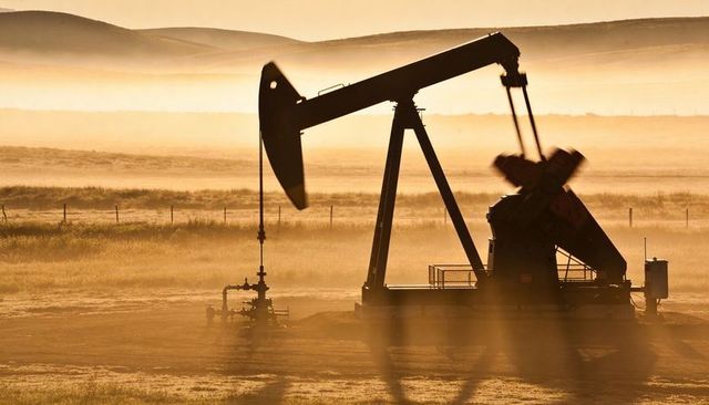 Pumpjack silhouette at sunrise over prairie haze, amber oil field, energy industry concept