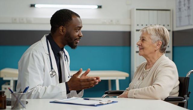 Black doctor consulting senior woman in wheelchair during compassionate clinical visit