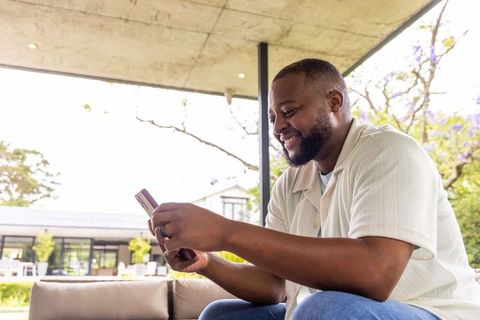 Smiling man using smartphone on outdoor patio sofa under modern concrete canopy