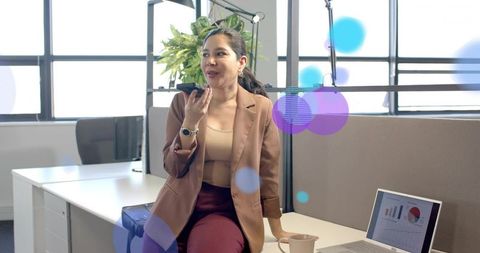 Professional woman speaking into smartphone at modern office desk with laptop charts
