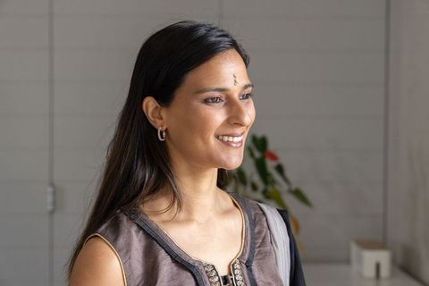 South asian woman smiling and looking right wearing embroidered tunic, bindi and gold hoops