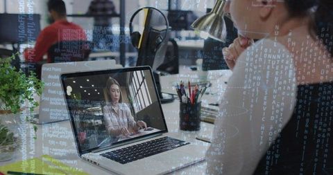 Mid-adult Asian woman watching remote colleague on laptop at modern coworking desk