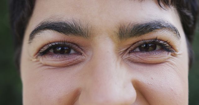 Close-up view of a person's smiling eyes showing thick eyebrows and expressive wrinkles, capturing a moment of genuine happiness and positive emotion. Ideal for use in marketing materials for skincare, happiness campaigns, emotional well-being content, or any project seeking to highlight joy and positive human expressions.