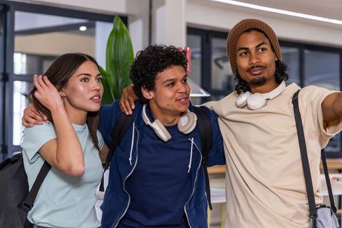 Diverse students laughing and posing on campus wearing backpacks and headphones