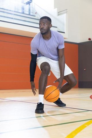 African american athlete dribbling basketball on indoor court crouching focused training