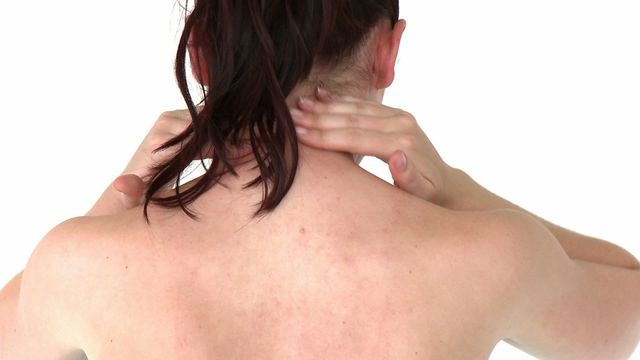 Back view of a woman massaging her neck, indicating tension relief. The posture and hand placement suggest self-care practices common for addressing headaches or stress. Ideal for wellness concepts, tutorials on effective relief techniques, or health and lifestyle blogs focusing on stress reduction through physical therapy.